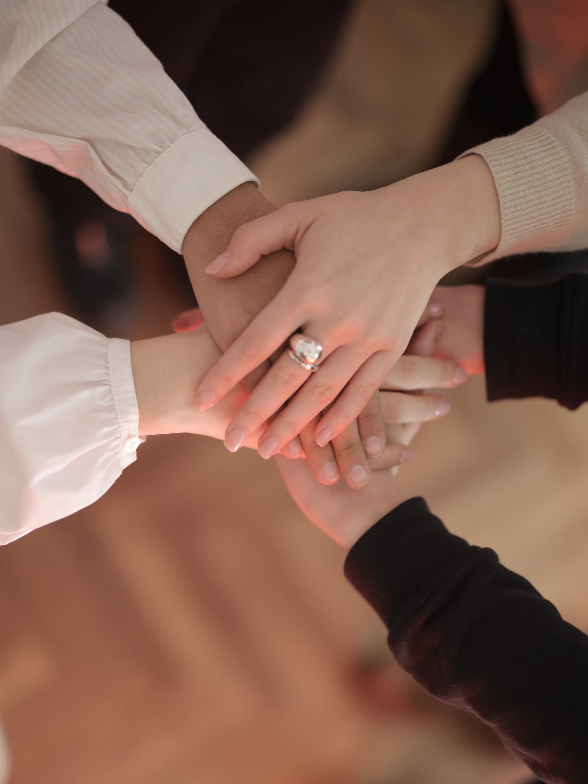 Top view of faceless friends in different clothes stacking hands together while standing on wooden floor indoor on sunny day